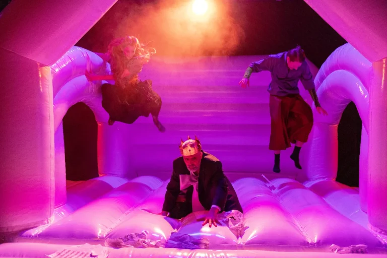 Frau Yamamoto ist noch da. Foto: Joseph Ruben Künstlerische Projektion des Marmolata Massivs auf ein Bühnenbild. Davor eine Schauspielerin in orangenem Anzug.