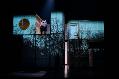 Theaterbühne mit einer Projektion von einem Haus und zwei Figuren darauf.